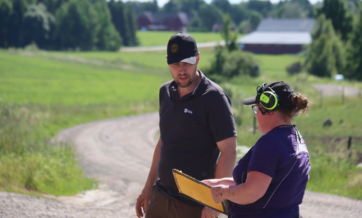 Två lantbrukare diskuterar i svenskt sommarlandskap.