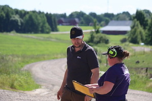 Två lantbrukare diskuterar i svenskt sommarlandskap.