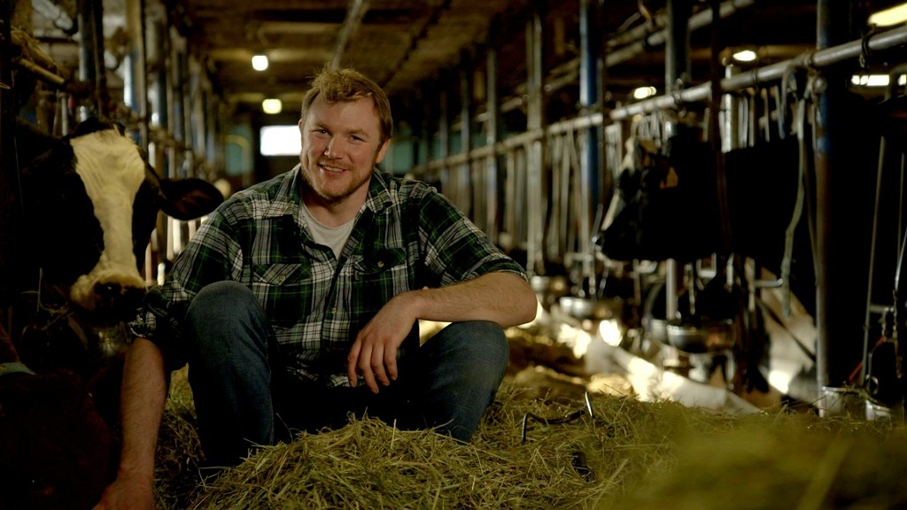 Anders Mood är en av mjölkbönderna i Bonde söker fru. Han sitter på huk på foderbordet klädd i en rutig skjorta.