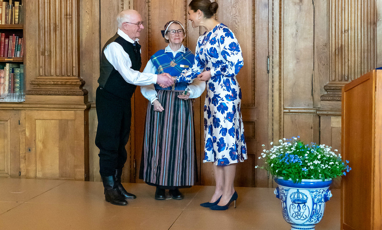 Ett äldre par i folkdräkt tillsammans med kronprinsessan Victoria i blåblommig klänning.
